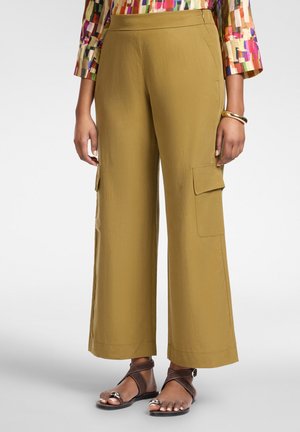 Weite, olivgrüne Cargo-Hosen mit Klappentaschen, getragen mit einem mehrfarbig gemusterten Langarmshirt und braunen Sandalen mit offenen Zehen.