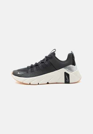 Čierno-biela športová teniska s hrubou podrážkou, šnurovacím dizajnom, malými logami Nike Swoosh blízko špičky a päty a ťahacími záložkami na jazyku a päte.