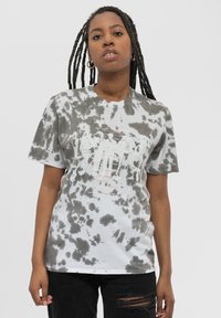 Gray and white tie-dye cotton t-shirt with a graphic print in red and black. Short sleeves, crew neck, and relaxed fit. Black ripped jeans.