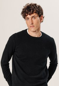 Schwarzer Rundhalsausschnitt-Pullover aus einem weichen Stoff. Verfügt über eine schmale Passform mit langen Ärmeln, minimaler Naht und einer glatten Textur.