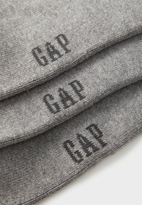 Calze grigie impilate, con un knit testurizzato. Logo nero "GAP" ben visibile su ogni calza. Design semplice, senza altri accenti notevoli.