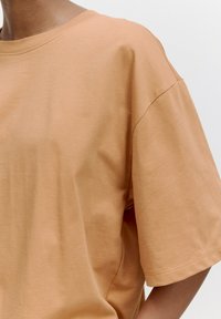 Korte mouwen, ontspannen fit t-shirt van lichtbruin katoen. Heeft een ronde halslijn en een soepele textuur, met een platte naaddetail op de mouwen.