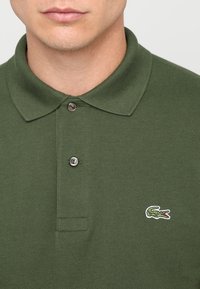 Mörkgrön polo skjorta i texturerad tyg, med klassisk krage, tvåknapps-knäppning och en liten broderad krokodil-logotyp.