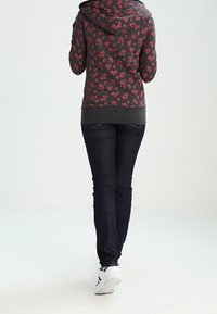 Grijze bloemenhoodie met een capuchon en geribde manchetten, gecombineerd met donkerblauwe skinny jeans en witte sneakers met zwarte accenten.