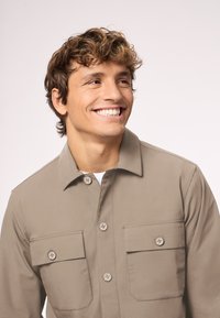 Khakifarbenes Hemd mit Knöpfen, zwei Brusttaschen, einem klassischen Kragen und einer glatten Textur. Verfügt über ein sauberes, elegantes Design und passende Knöpfe.