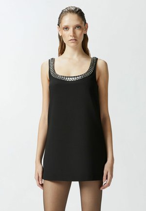 Robe noire sans manches avec un décolleté carré, ornée d'une chaîne métallique décorative autour du col. Design lisse et minimaliste.