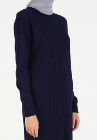 Abito lungo a maniche lunghe in maglia di colore blu navy, con design a treccia testurizzata sul davanti e polsini a costine. Tessuto morbido e vestibilità rilassata.