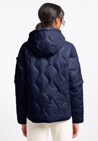 Marineblauwe gewatteerde pufferjack met capuchon, voorzien van een golvend patroon en subtiele glans. Lange mouwen en zijzakken zijn zichtbaar.