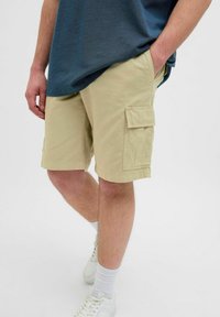 Beżowe szorty cargo z bawełny, z bocznymi kieszeniami i luźnym krojem, w połączeniu z szarym T-shirtem i białymi trampkami.