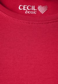 T-shirt en coton rouge avec un col rond, de couleur unie et un logo subtil avec un design en forme de cœur en métal argenté au niveau du col.
