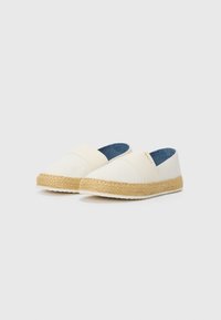 White canvas espadrilles with a jute rope sole, featuring a smooth texture and a blue interior. A small logo is embossed on the side.