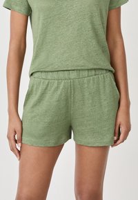 Zielony, krótkozapiany top z miękkiego, teksturowanego materiału, połączony z dopasowanymi zielonymi szortami z elastycznym pasem. Oba elementy mają luźny krój.