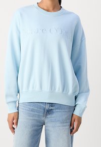 Light blue sweatshirt featuring a crew neckline and embroidered "Marc O'Polo" logo. Soft fabric with a relaxed fit and ribbed cuffs.