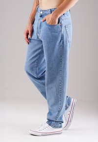 Helle blaue Jeans mit einem lockeren Schnitt, ausgestattet mit einem klassischen Fünf-Taschen-Design, Metallknöpfen und kontrastierenden Nähten. Getragen mit weißen Sneakers.