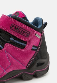 Różowe zamszowe buty turystyczne z czarnymi akcentami z siatki, z niebieską podszewką, kontrastowym przeszyciem i paskiem na rzep. Widoczny detal logo.