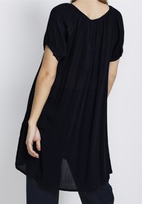Túnica de color azul marino oscuro hecha de tela ligera, con escote en V, mangas cortas remangadas y un ajuste holgado con aberturas laterales.