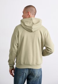 Hooded sweatshirt in light olive green, made of soft fabric, featuring a kangaroo pocket, ribbed cuffs, and waistband; simple, relaxed fit.