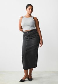 Sorte denim midi-skørt med lige snit, der har for sømme og høj talje. Kombineret med en tætsiddende grå top og sorte hæle.