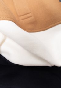 Gelaagd stof met bruine, crèmekleurige en marineblauwe secties. Soepele textuur met gestikte randen, die kleurvlakken en een schoon ontwerp laat zien.