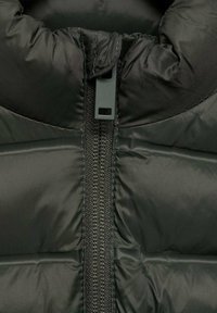 Čierna páperová bunda s vysokým golierom. Obsahuje kovový zips so textilným lemovaním a prešívané časti na izoláciu.