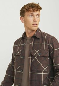 Bruine geruite shirtjas met een knoopsluiting, twee borstzakken en contrasterende crèmekleurige en donkere lijnen. Zacht, gestructureerd stof.