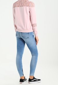 Rosa sweatshirt med spetsdetaljer på axlar och ärmar, i kombination med ljusblå skinny jeans och svarta sneakers med vita sulor.