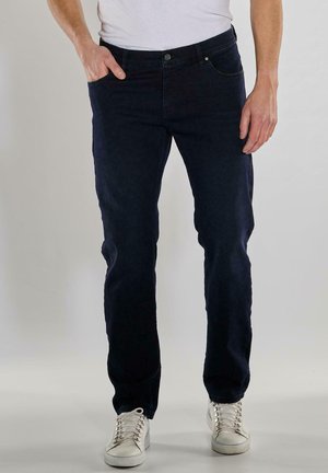 Dark blue denim jeans with a straight cut, featuring five pockets, a button-fly closure, and subtle stitching details. Worn with white sneakers.