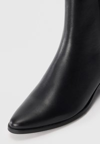 Stivale alla caviglia in pelle nera con punta affusolata, design elegante e superficie liscia. Minimi dettagli in metallo e tacco basso e rotondo.