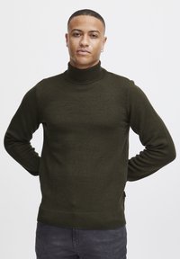 Pulover cu guler înalt de culoare verde închis, realizat dintr-un material tricotat texturat, având o siluetă ajustată și mânici și tiv de tip dantelat.