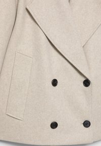Beżowy płaszcz wełniany z szerokimi klapami, czterema czarnymi guzikami ułożonymi w stylu dwurzędowym oraz pojedynczą prostokątną boczną kieszenią.