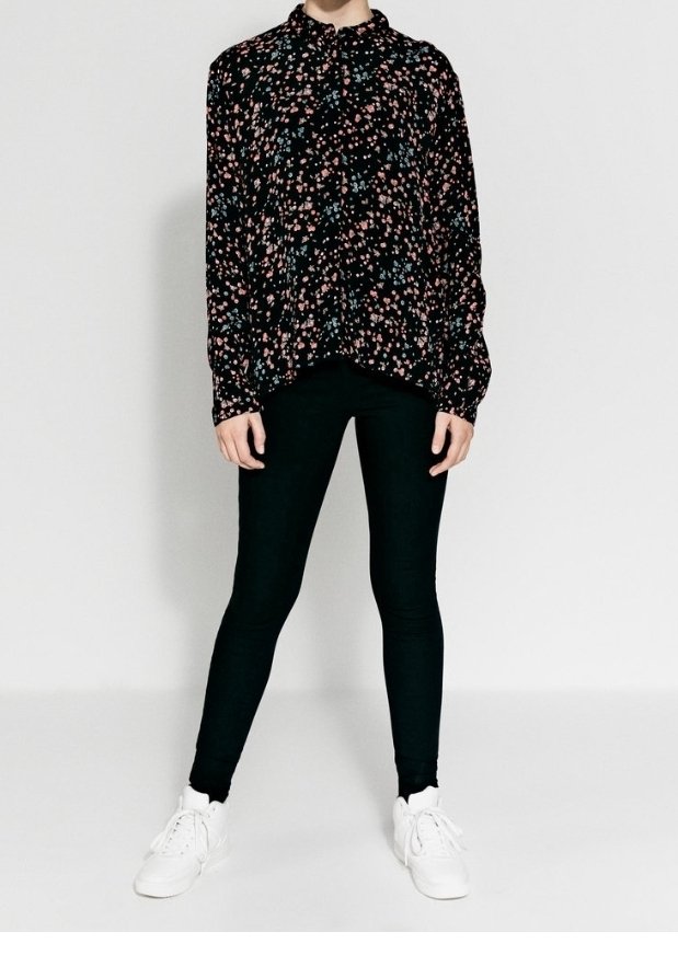Svart blommig blus med rosa och blå mönster, har långa ärmar och en krage, tillsammans med svarta leggings och vita sneakers.