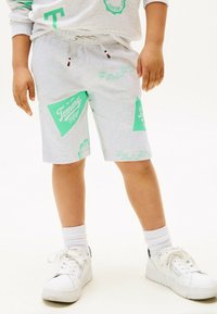 Lichtgrijze shorts met turquoise grafische prints, trekkoord in de taille en zijzakken. Gecombineerd met witte sneakers en geribbelde witte sokken.