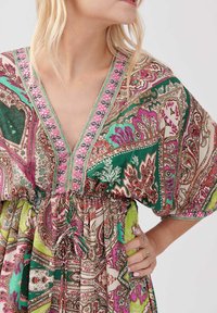 Kaftan multicolore avec un col en V, ornée de motifs paisley complexes en vert, rose et brun, resserrée à la taille par un cordon de serrage.