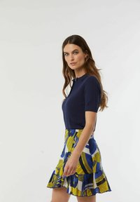 Navy geribbelde top met korte mouwen, gecombineerd met een kleurrijke minirok met een patroon van geel en blauw, met een geschulpte zoom.