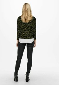 Grön leopardmönstrad jacka med långa ärmar, lager på lager över en vit skjorta, tillsammans med svarta läderleggings och ankelboots.