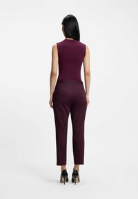 Burgundowa bezrękawnikowa bluzka o ryflowanej fakturze w połączeniu z burgundowymi dopasowanymi spodniami, dopełniona czarnymi szpilkami.