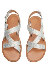 Söta sandaler med silverglitter, korskedjor och en brun gummisula samt justerbar ankelsnörning. Slät ovandel och öppen tå-design.