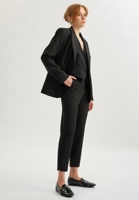 Zwart tailormade pak met een getailleerde blazer en cropped broeken. De ensemble is gecombineerd met glanzende zwarte loafers.