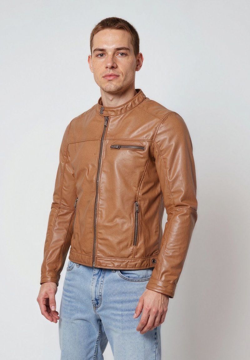 Hnědá kožená bunda s měkkým límcem, předním zipem, dvěma bočními kapsami a náprsní kapsou. Hladká textura a přiléhavý design.