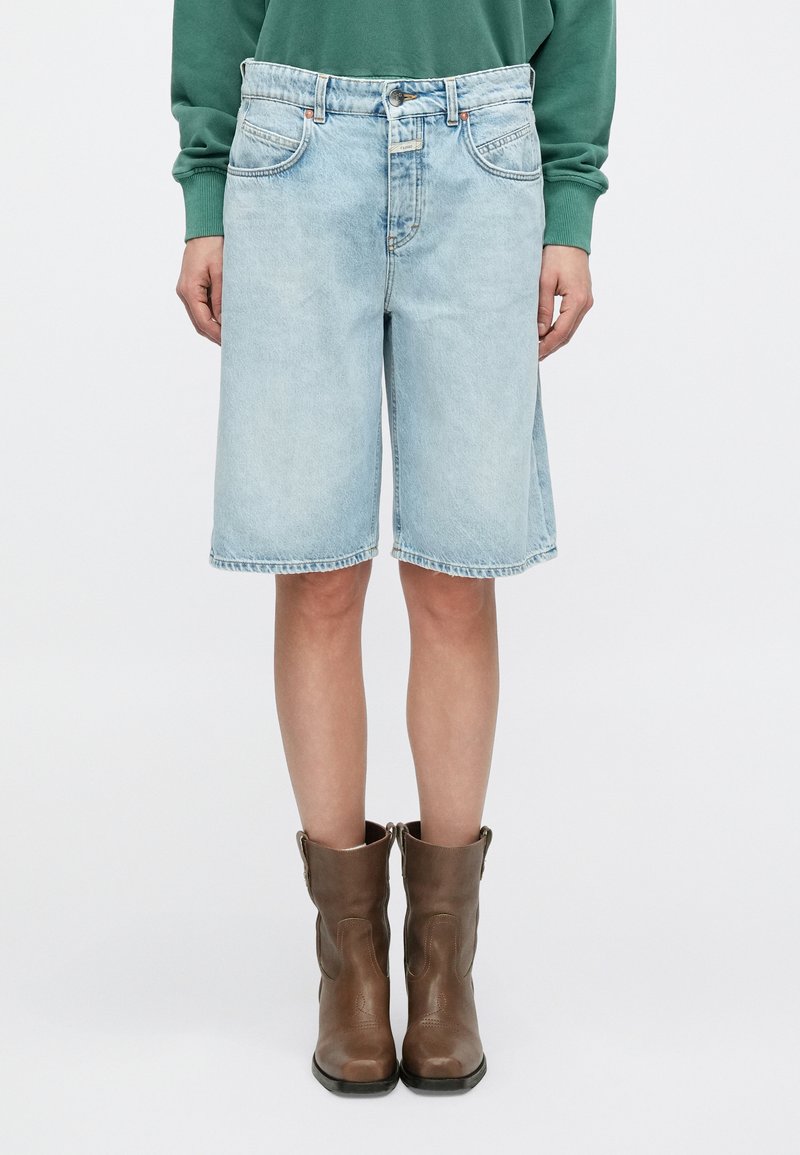 Ανοιχτό μπλε τζιν σορτς Βερμούδα με ευθεία κοπή, πέντε τσέπες και ορατή ραφή. Συνδυασμένα με καφέ δερμάτινα μποτάκια αστραγάλου.