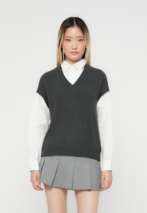 Gilet gris en tricot avec un col en V, superposé sur une chemise blanche à col ; associé à une jupe plissée grise. Design minimal avec des lignes épurées.