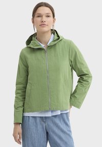 Veste verte légère avec capuche, fermeture éclair à l'avant et deux poches latérales. Texture lisse, coupe courte et détails de coutures visibles.