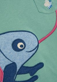 Groene katoenen t-shirt met een blauw geborduurd visontwerp, een roze gestikt lijntje en een klein geborduurd insect op de zak.