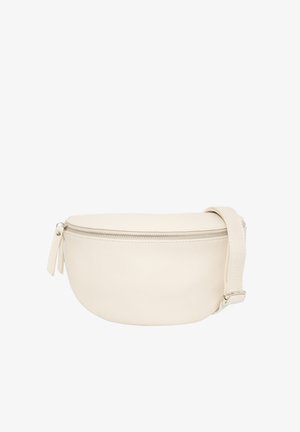 Jeune femme aux longs cheveux bruns portant un haut noir à manches longues et un pantalon en cuir, avec un sac bandoulière beige à fermeture éclair.