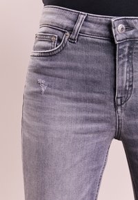 Jeans de mezclilla gris con una cintura de altura media, bolsillo frontal con un botón plateado y una sutil marca de desgaste en el muslo.