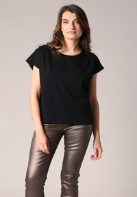 Zwarte top met korte mouwen en een relaxte pasvorm, gecombineerd met glanzende metallic bronzen slim-fit broek. Eenvoudig ontwerp en lichtgewicht stof.
