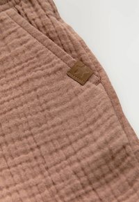 Tissu brun texturé avec un motif en grille, avec une étiquette en cuir beige dans le coin. Apparence douce et légèrement froissée.