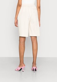 Beige šortky po kolena s elastickým pasem a volným střihem. Spárované s růžovými otevřenými lodičkami s úzkým podpatkem.