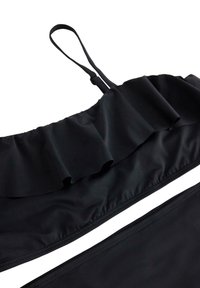 Musta bikinit-setti, jossa on röyhelöpäällys ja säädettävät olkaimet. Kangas on sileä ja venyvä, ja siinä on yksinkertainen, kuvioton muotoilu.