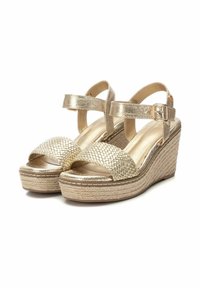 Sandalias de cuña doradas con tiras metálicas trenzadas, parte superior lisa, correa ajustable en el tobillo y plataforma texturizada similar al corcho.